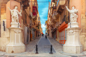 The traditional Maltese street stairs with corners of houses, decorated with statues of saints St. John and St. Paul and building with colorful balconies in Valletta, Capital city of Malta