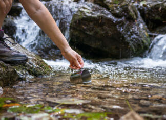 Pomanjkanje vode v Sloveniji: »Sleherni v državi ima pravico do zdrave in pitne vode.« Thirsty hiker scoops fresh water into cup from stream in mountains. Refreshment during hiking in nature