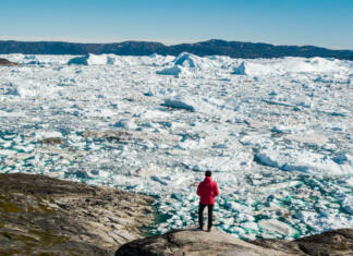 Arktika se segreva še hitreje, kot smo mislili Travel in arctic landscape nature with icebergs - Greenland tourist man explorer - tourist person looking at amazing view of Greenland icefjord - aerial drone image. Man by ice and iceberg, Ilulissat.