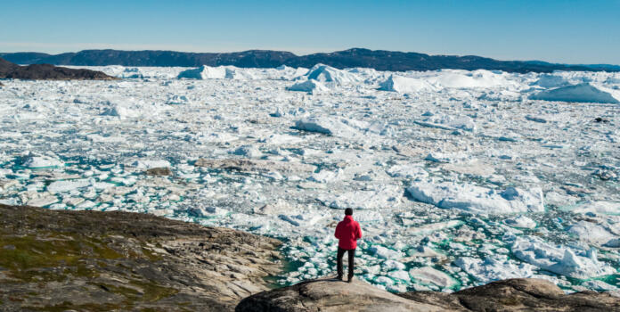 Travel in arctic landscape nature with icebergs - Greenland tourist man explorer - tourist person looking at amazing view of Greenland icefjord - aerial drone image. Man by ice and iceberg, Ilulissat.