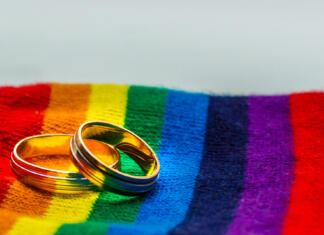 Izšli so novi obrazci listine za sklenitev zakonske zveze Two wedding rings on the fabric colors of the rainbow. Concept same-sex marriage.