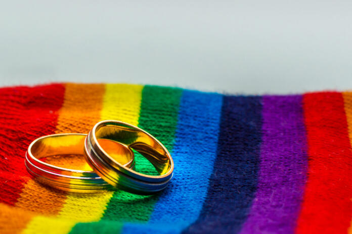 Two wedding rings on the fabric colors of the rainbow. Concept same-sex marriage.