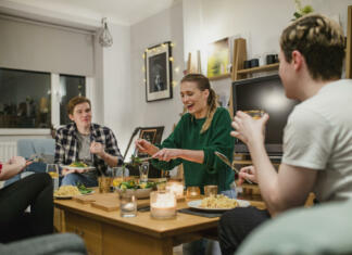 Razpis za ponudnike študenstke prehrane za leti 2023 in 2024 Two young couples are having a dinner party and one woman is laughing while serving salad.