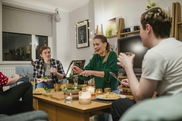 Two young couples are having a dinner party and one woman is laughing while serving salad.
