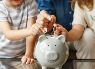 Denarna pomoč študentskim družinam v letu 2022/23 Unrecognizable senior man and kids putting coins into piggy bank on table at home together