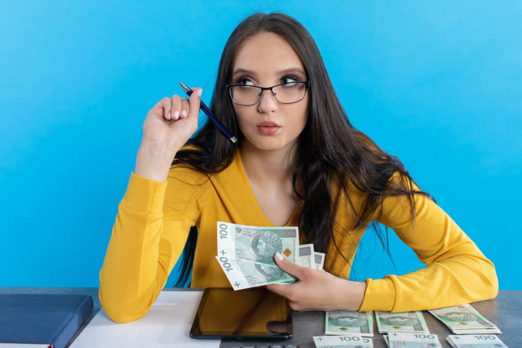 While counting money, a young woman uses a calculator and a tablet to check the stock exchange.