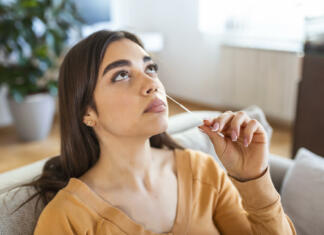 Študenti in dijaki dobijo teste za samotestiranje woman using cotton swab while doing coronavirus PCR test at home. Woman using coronavirus rapid diagnostic test. Young woman at home using a nasal swab for COVID-19.