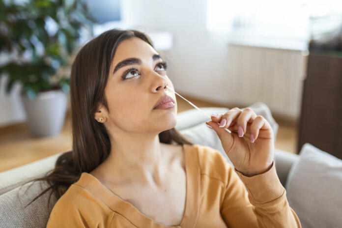 woman using cotton swab while doing coronavirus PCR test at home. Woman using coronavirus rapid diagnostic test. Young woman at home using a nasal swab for COVID-19.