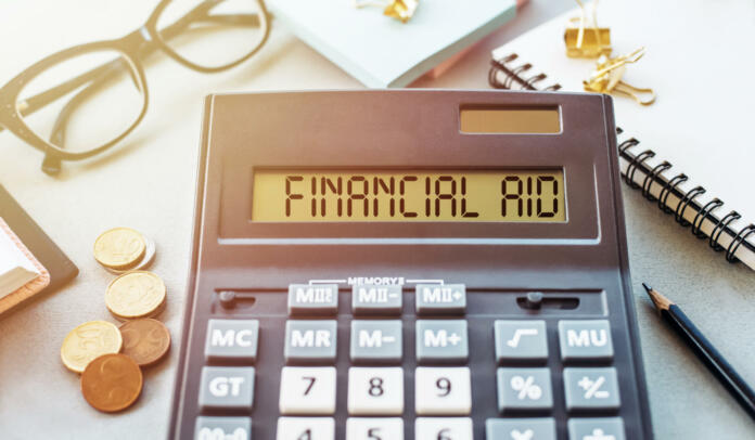 Word FINANCIAL AID written on calculator on office table.