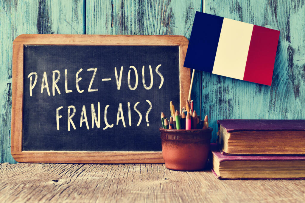a chalkboard with the question parlez-vous francais? do you speak french? written in french, a pot with pencils and the flag of France, on a wooden desk