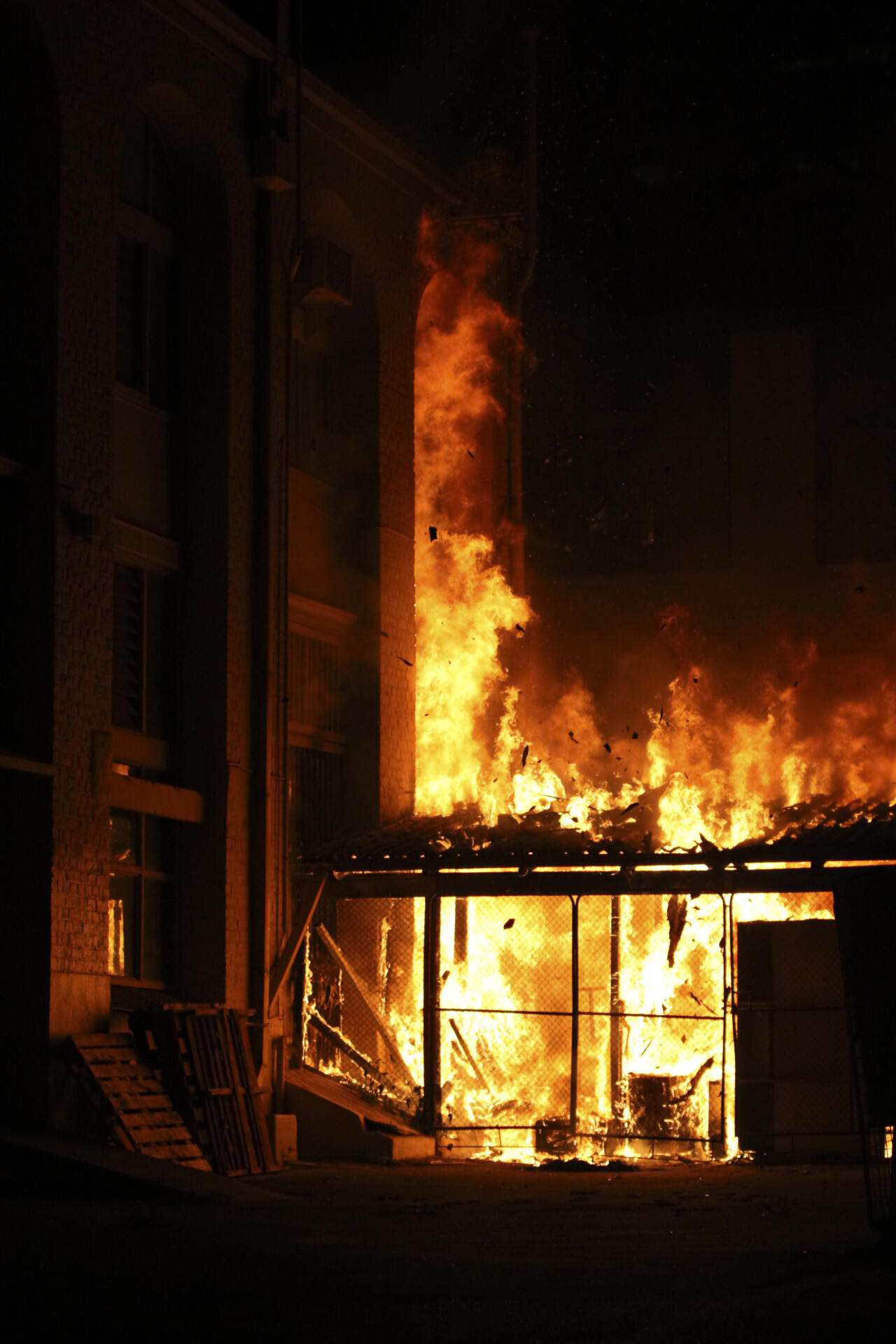 A shed and building burning at night.