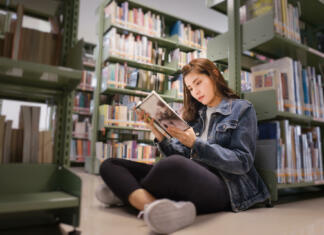 Učenje v knjižnici Asian female student sitting on floor in the library, Open and learning textbook from bookshelf in the International College/University Library.
