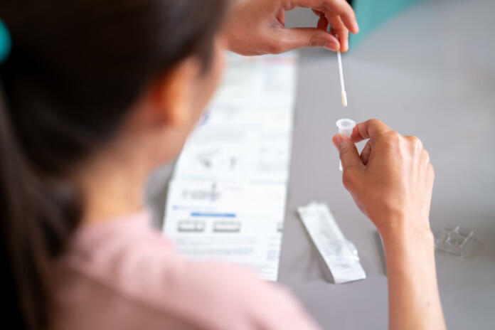 Asian woman using rapid antigen test kit for self test COVID-19 epidemic at home. Adult female place the fabric tip of the swab in the extraction tube and rolling around the tube. COVID-19 pandemic protection concept.