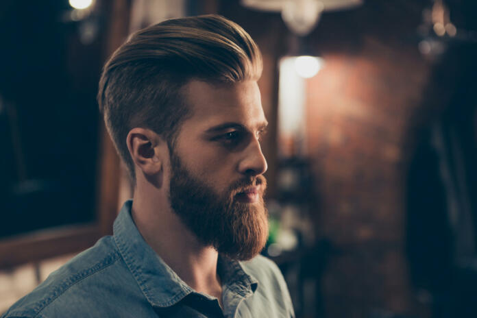 Barbershop concept. Profile side portrait of attractive severe brutal red bearded young guy. He has a perfect hairstyle, modern stylish haircut