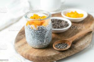 Chia pudding in glass jar with almond milk and mango on wooden cut board, white background - healthy superfood vegan, dairy free breakfast