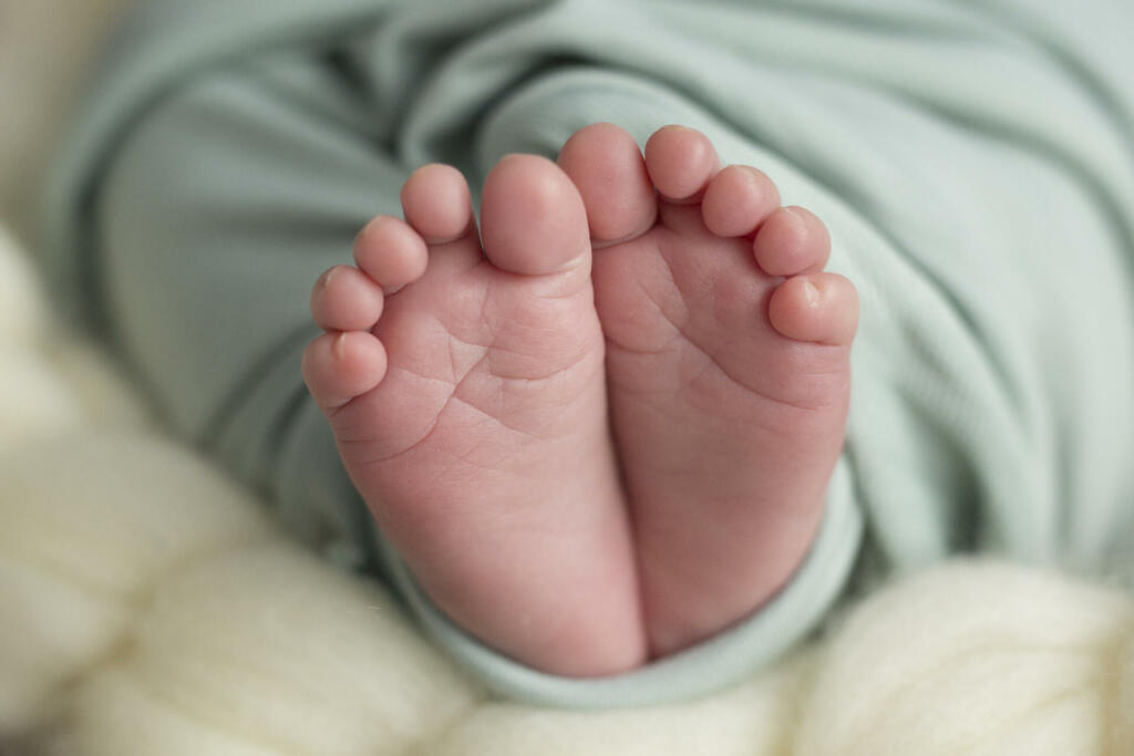 Children's sweet feet wrapped in a turquoise blanket on beige background, close up.