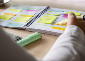 USPEŠNI ŠTUDENTJE PRAVA Close-up of agenda organize with color-coding sticky notes for time management. Productive schedule for appointments and reminders. Hand holding a yellow highlighter marker. Organization and planning