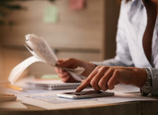 Kaj so minimalni življenjski stroški? Close up of businesswoman going though finances and using mobile phone as calculator.