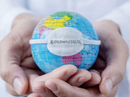 closeup of a caucasian doctor man holding a world globe with a protective mask with the word coronavirus written in it