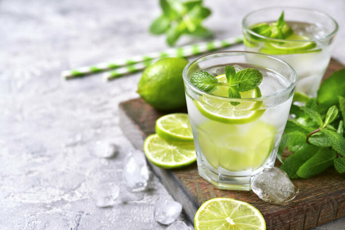 Cold refreshing summer lemonade mojito in a glass on a grey concrete or stone background.