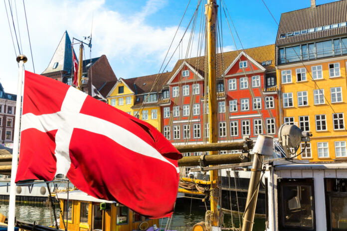 Copenhagen iconic view. Famous old Nyhavn port in the center of Copenhagen, Denmark during summer sunny day with Denmark flag on the foreground