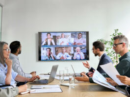 Diverse company employees having online business conference video call on tv screen monitor in board meeting room. Videoconference presentation, global virtual group corporate training concept.
