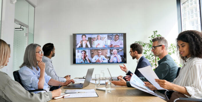 Diverse company employees having online business conference video call on tv screen monitor in board meeting room. Videoconference presentation, global virtual group corporate training concept.