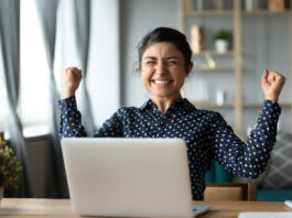Euphoric young indian girl student winner celebrate victory triumph sit at home desk with laptop computer win online fortune feel excited get new job opportunity good exam result great news concept