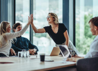 Interno komuniciranje Female professional giving a high five to her colleague in conference room. Group of colleagues celebrating success in a meeting.
