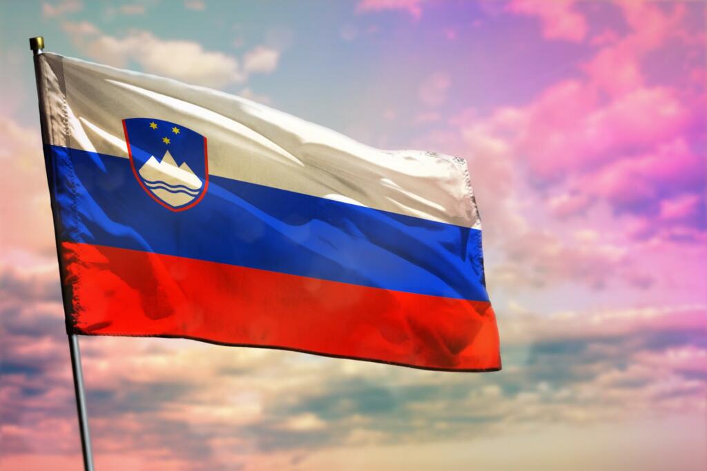 Fluttering Slovenia flag on colorful cloudy sky background. Slovenia prospering concept.