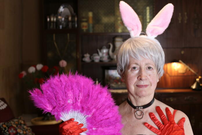 Fun senior woman with bunny ears and feathers hand fan.