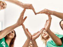 Group of young volunteers woman smiling happy make heart symbol with hands together at charity center.