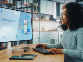 Handsome Black Female is Using Desktop Computer that Shows Welcome Page of a Popular Social Network. Freelance Woman Working Over the Internet as a Social Network Marketer.