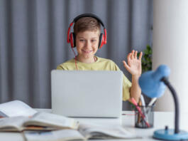 Happy elementary student waving to someone while having an online class over computer at home. Copy space.