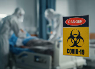 Miti in resnice o okužbi s Koronavirusom Hospital Coronavirus Emergency Department Ward: Doctors wearing Coveralls, Face Masks Treat, Cure and Save Lives of Patients. Focus on Biohazard Sign on Door, Background Blurred Out of Focus