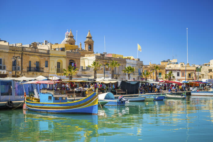 Malta - Marsaxlokk market with traditional Luzzu fishing boats on a beautiful summer day withblue sky and green sea