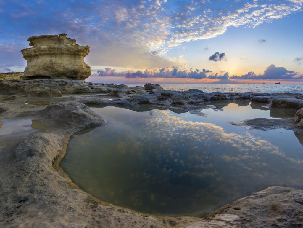 Malta - Sunrise at St.Peter's Pool with huge rocks of Delimara and reflections of the sky and clouds