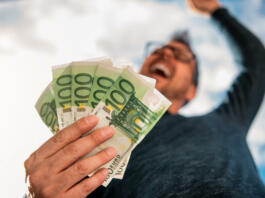 Man with glasses wearing blue shirt. and holding stack of money.
