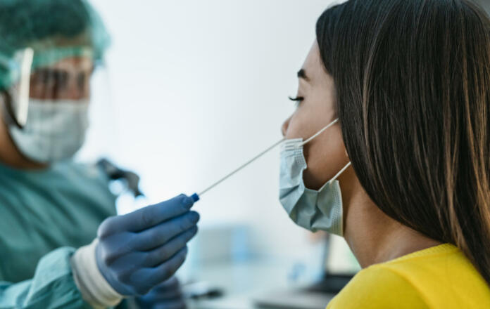 Medical worker wearing personal protective equipment doing corona virus swab on female patient - Covid19 test and health care concept