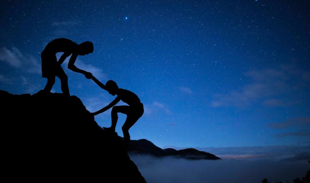 Dečka ponoči plezata na skalo in en pomaga priti na vrh drugemu