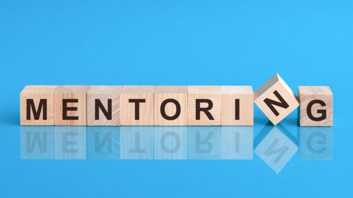 mentoring word written on wood block. reduction word is made of wooden building blocks lying on the yellow table. Business concept