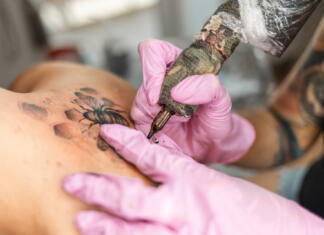 Tetovaža, da ali ne Modern youth culture. Close up of hands in pink latex gloves makes a tattoo design at client's back. Concept of world tattoo day.