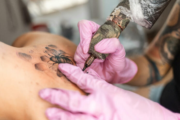 Modern youth culture. Close up of hands in pink latex gloves makes a tattoo design at client's back. Concept of world tattoo day.