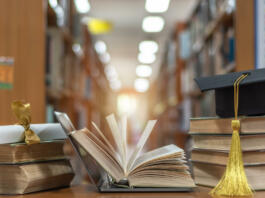 Online education course, E-learning class and e-book digital technology concept with pc computer notebook open in blur school library or classroom background among old stacks of book, textbook