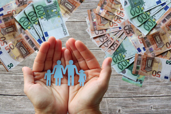 Paper family in hands on wooden background with euro banknotes