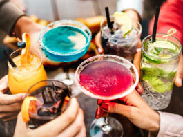 People hands toasting multicolored fancy drinks - Young friends having fun together drinking cocktails at happy hour - Social gathering party time concept on warm vivid filter