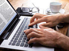 Person's Hand Typing On Laptop Over Wooden Desk