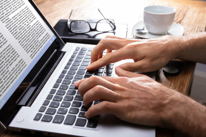 Person's Hand Typing On Laptop Over Wooden Desk