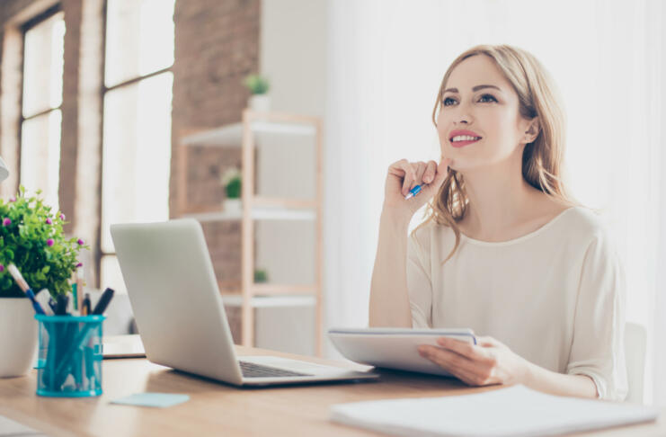 Portrait of young beautiful thoughtful lady sitting at the table working with laptop on writing down new ideas