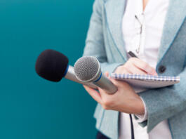Reporter or TV journalist at news conference, holding microphone and writing notes